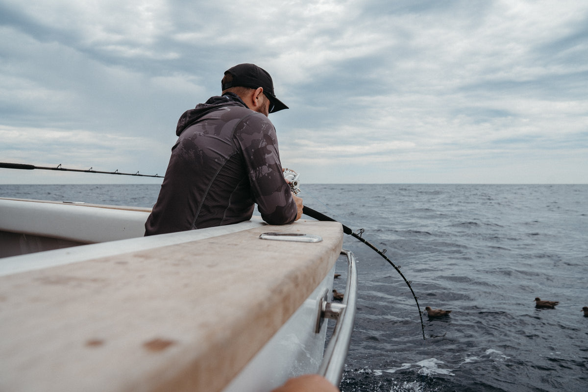 Angler in a Pelagic hooded shirt leans over the gunwale fighting a fish