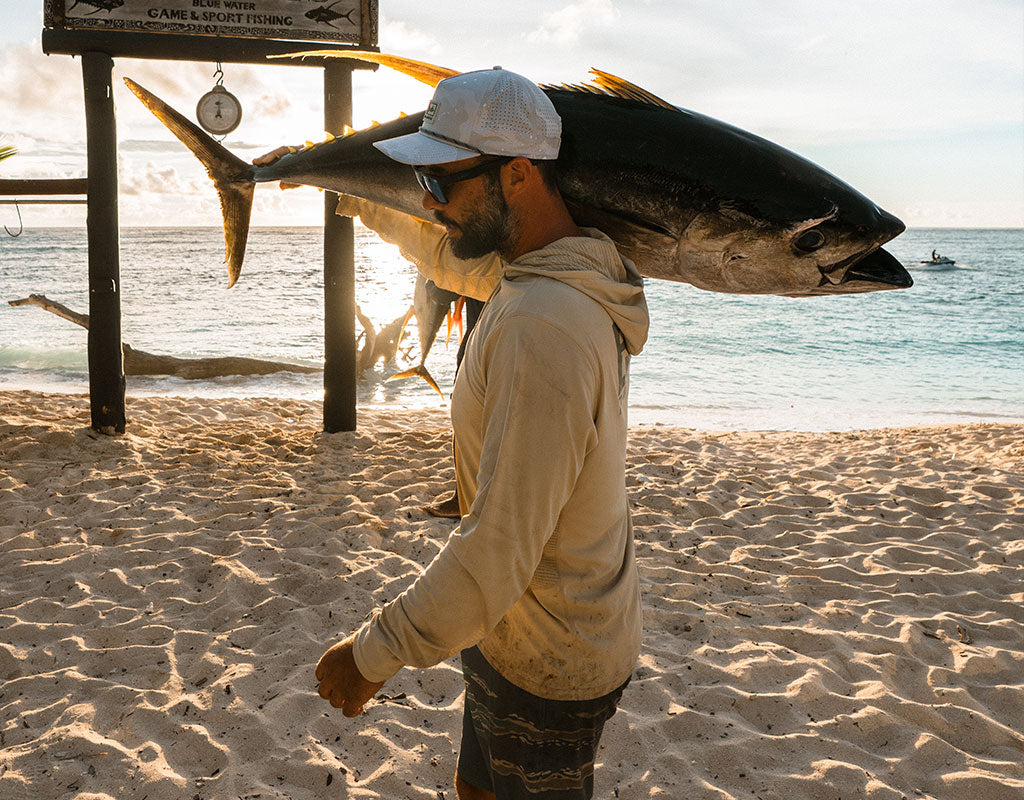Man carrying a tuna on his shoulder up the beach, wearing Pelagic gear in Sand